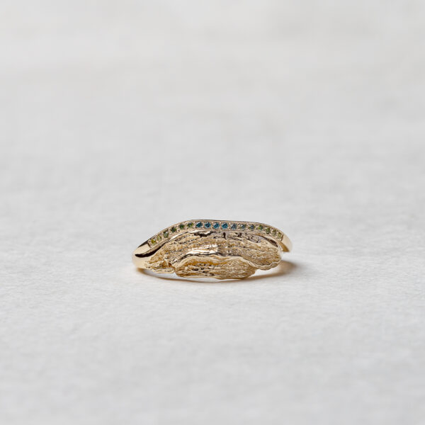 Close-up of the Ocean Wave ring with a row of naturally colored diamonds, transitioning from yellow to green to deep blue, delicately set in a strip of recycled 14k gold