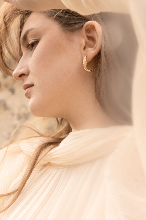 Model wearing handcrafted gold ocean wave earrings